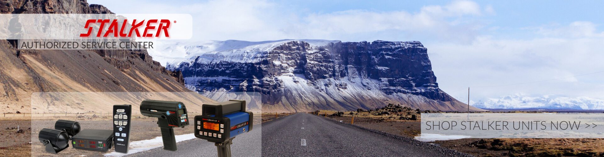 A road with mountains in the background and a blue suitcase on the side.