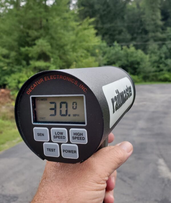 A hand holding up a speed gun on the side of a road.